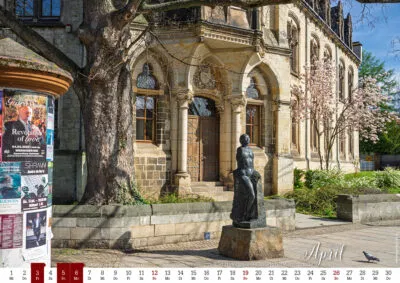 Statue vor historischem Gebäude (GHG) mit Baum und Plakatsäule.